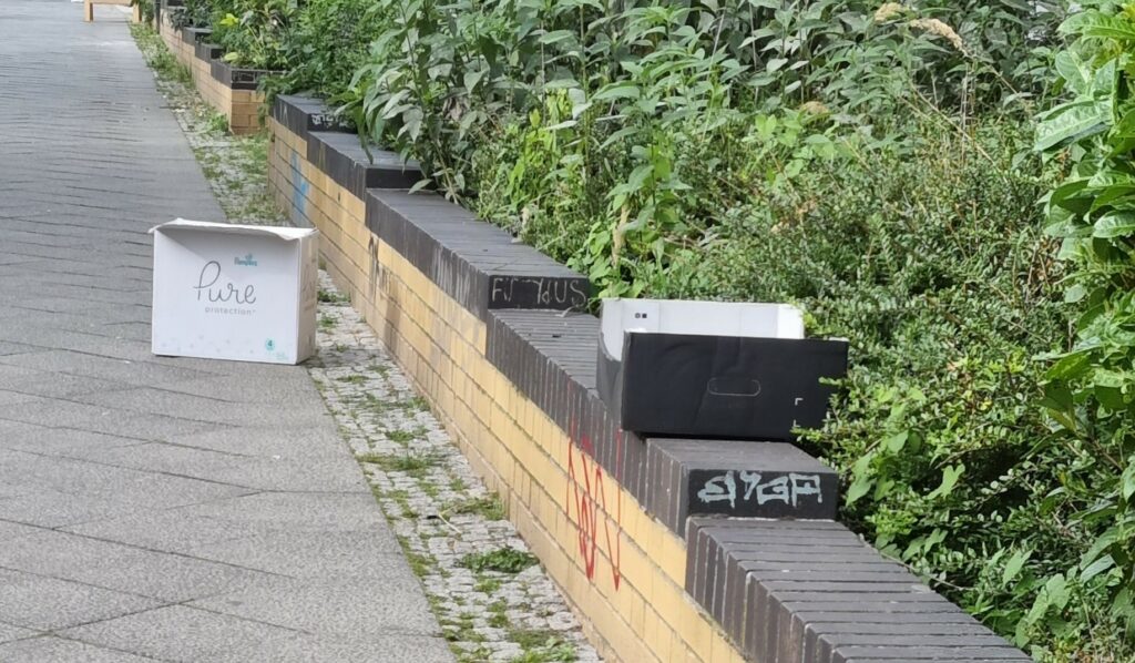 Blick die Straße hinauf auf zwei "Zu-Verschenken"-Kartons.